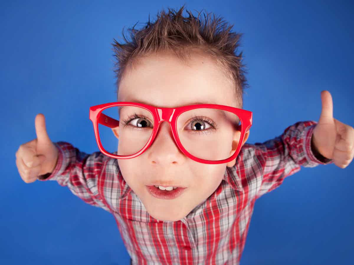 Boy with large red glasses and red checked shirt with both his thumbs up looking at the camera