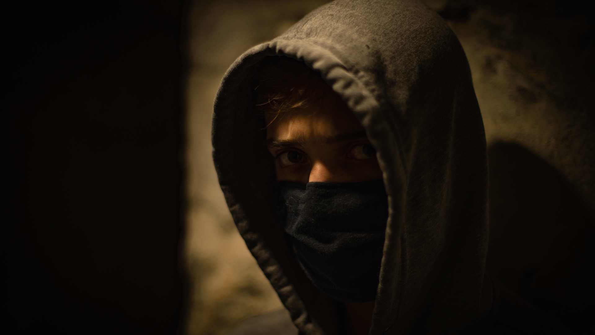 Boy wearing a hooded top and a black half face mask in a darkened area