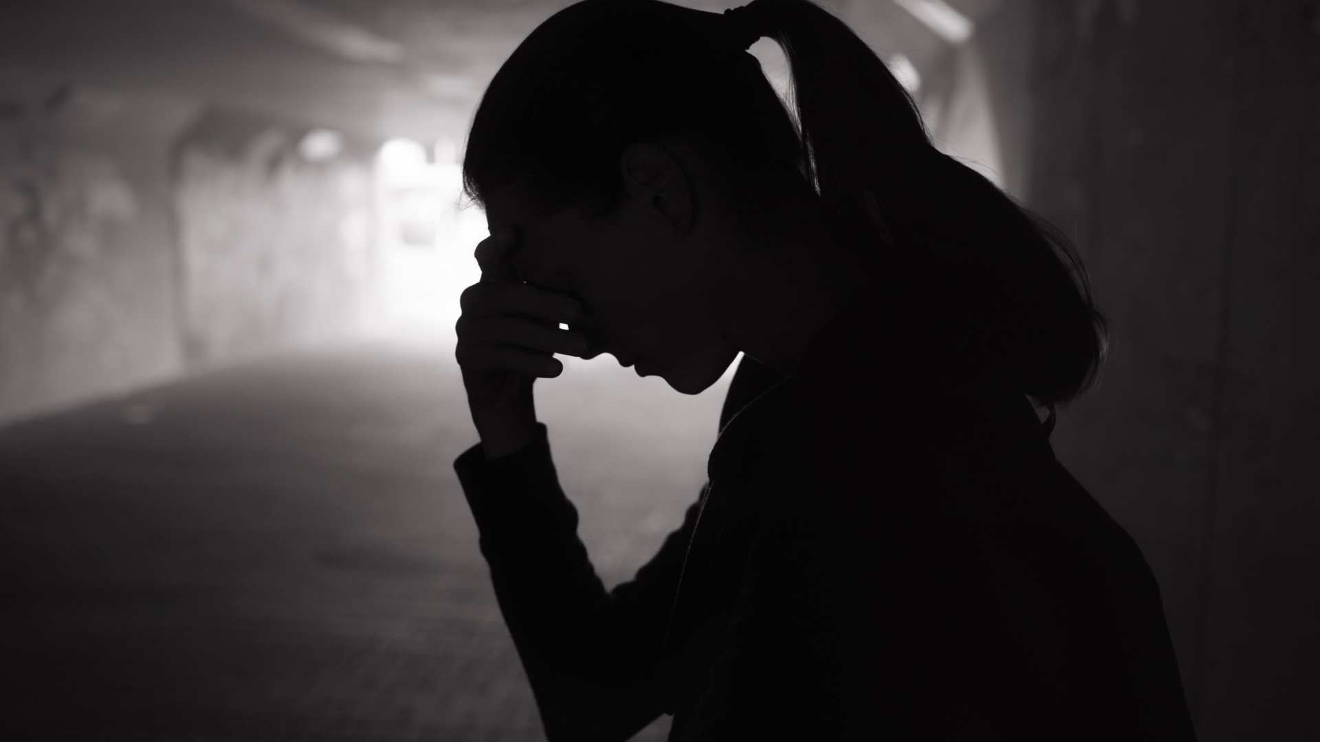 Silhouette of a girl with her head in her hands in a dark tunnel